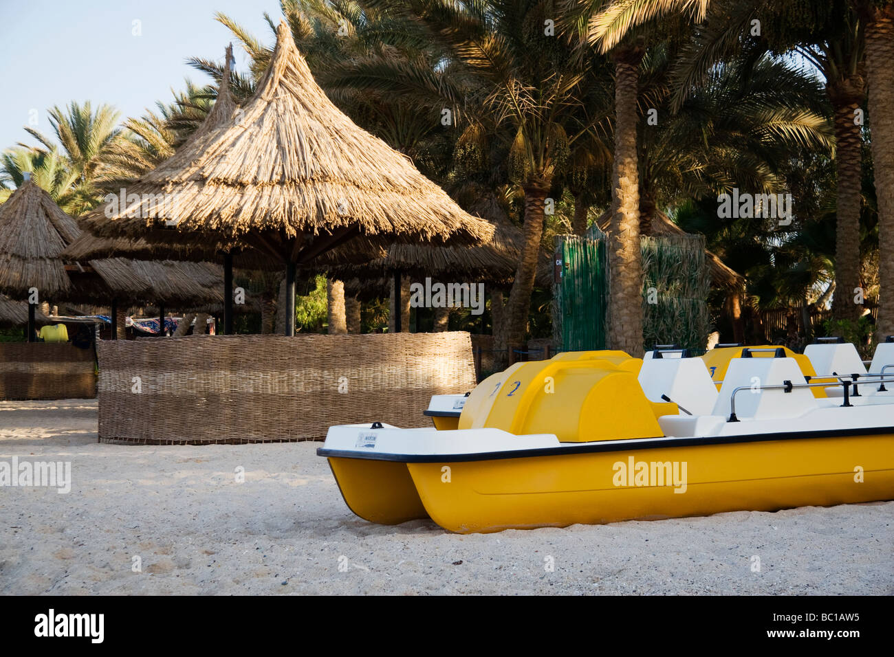 Gelben Tretboote und strohgedeckten Sonnenschirmen an einem tropischen Palmen gesäumten Strand Stockfoto