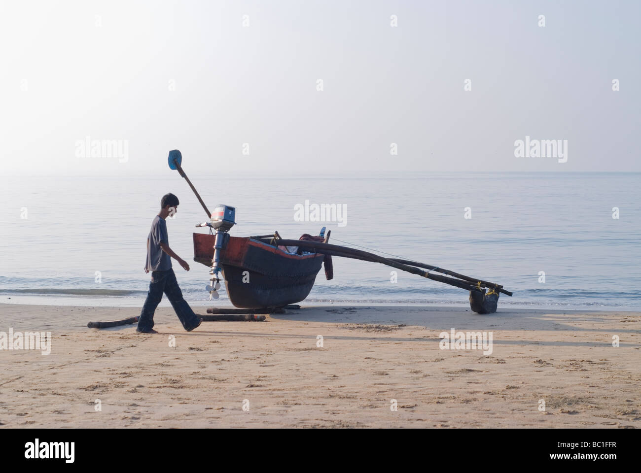 Indische Person zu Fuß entlang einem traditionellen Boot (aus einem Baumstamm gefertigt, und für den Fischfang eingesetzt). Palolem Beach, Goa, Indien. Stockfoto