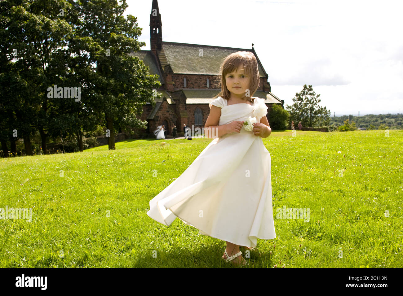 Ein kleines Mädchen als Brautjungfer steht eine Kirche nach einer Hochzeit. Stockfoto