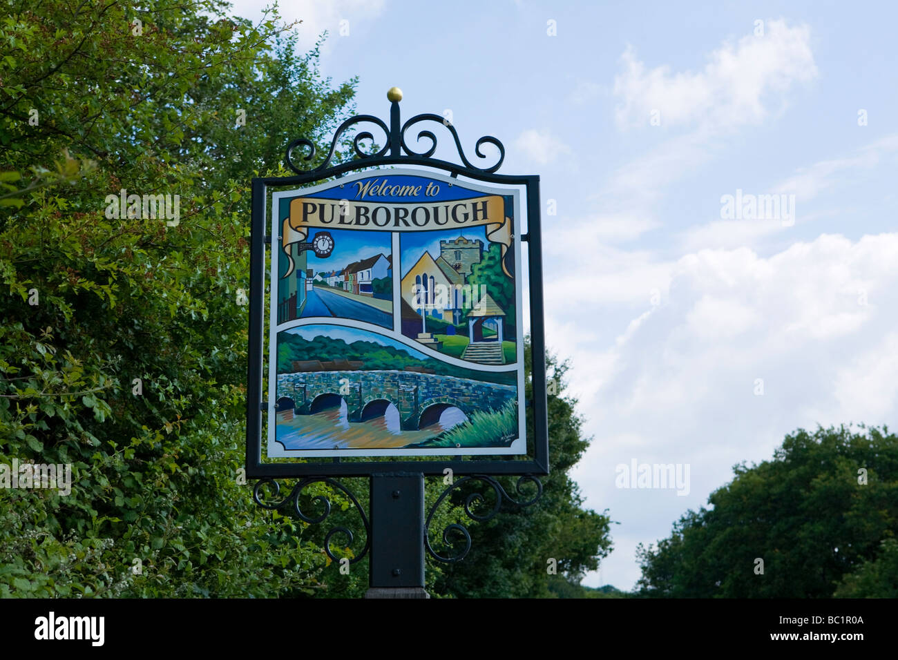 Holz und Metall Pulborough Ortsschild mit Stopham Brücke, Main Street und die Pfarrkirche der Heiligen Maria. West Sussex, England, Großbritannien Stockfoto