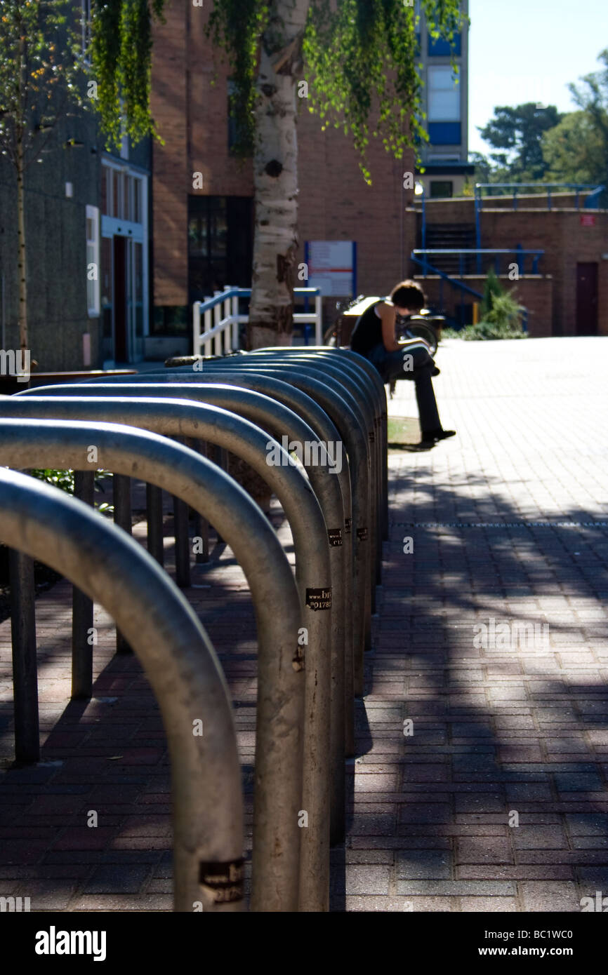 Ein Student, ein Buch draußen in der Sonne auf dem Gipsy Lane-Campus der Oxford Brookes University, Oxford. Leere Fahrradständer Stockfoto