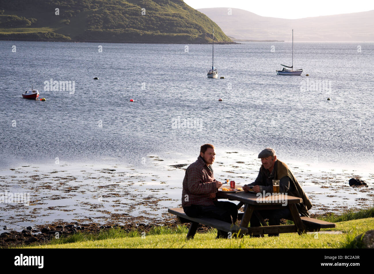 Zwei Männer trinken an einem Picknicktisch, Stein, Isle Of Skye, innere Hebriden, Westküste von Schottland, UK Stockfoto