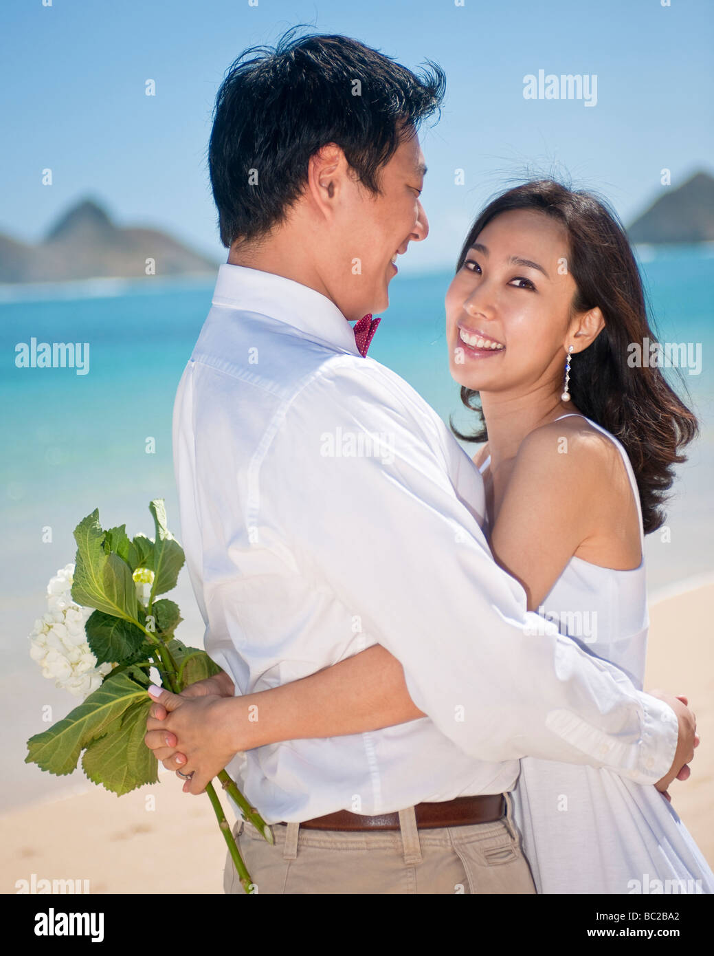 Asiatische Braut und Bräutigam umarmen und lachen, als sie ihre mit einem Spaziergang am Strand von Lanikai in Hawaii Flitterwochen Stockfoto