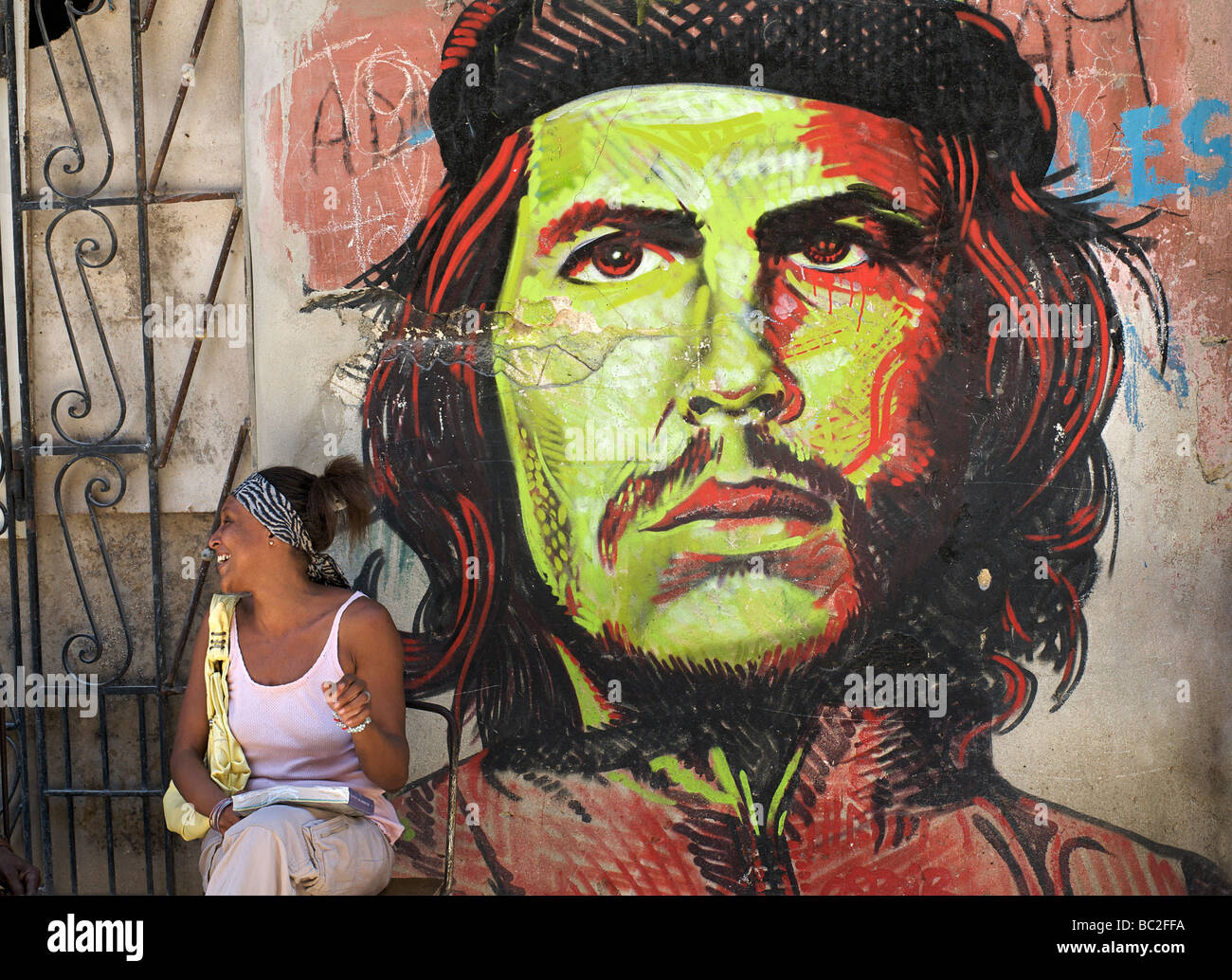 Kubanische Frau sitzt neben einer Wandmalerei des legendären Revolutionärs Che Guevara, Havanna, Kuba Stockfoto