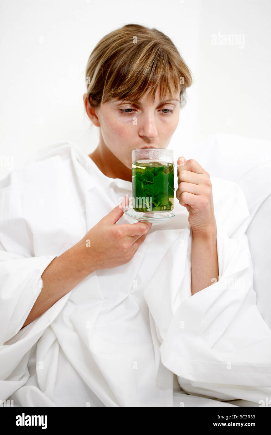 Frau im Bett hat eine Erkältung Halsschmerzen Getränke ein heiße Pfefferminztee aus Frech Minze Blätter Stockfoto