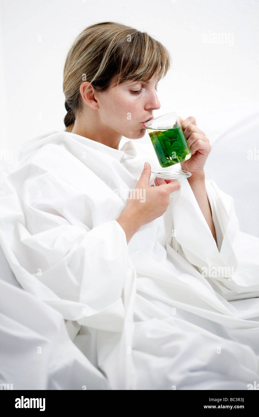 Frau im Bett hat eine Erkältung Halsschmerzen Getränke ein heiße Pfefferminztee aus Frech Minze Blätter Stockfoto