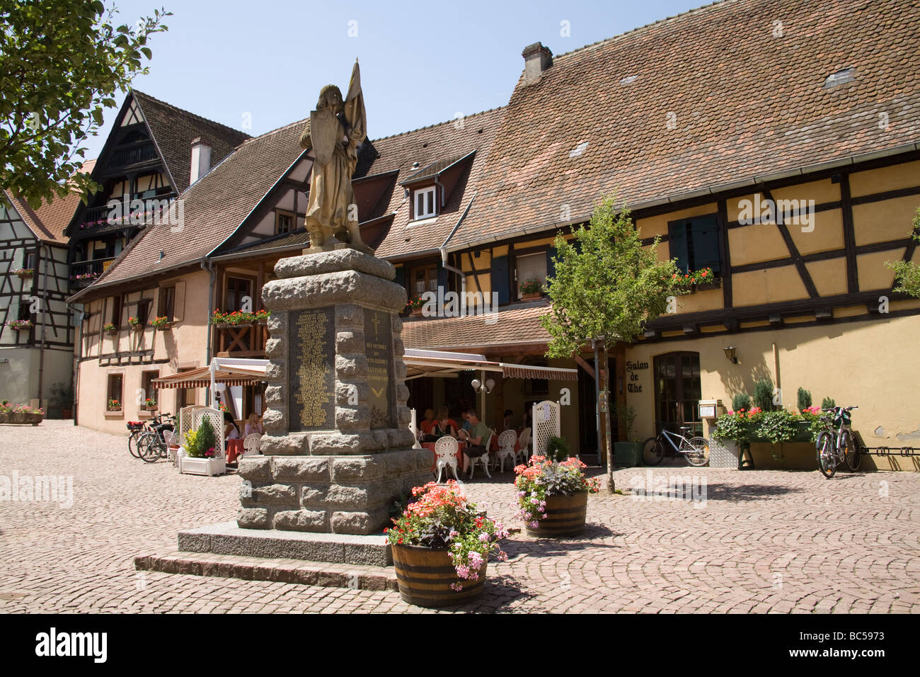 Eguisheim Elsass Frankreich EU Kriegerdenkmal und Freiluft-Café in einem Quadrat des mittelalterlichen Dorfes an einem perfekten Frühlingstag Stockfoto