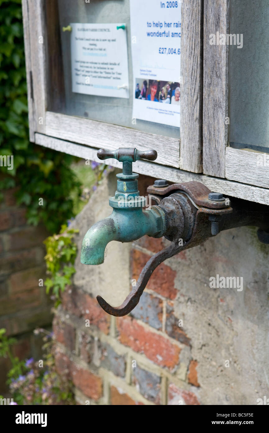 Öffentlicher Wasserhahn mit Haken darunter zum Aufhängen eines Griffs unter dem Hinweises Brett in Slaugham Village West Sussex UK Stockfoto