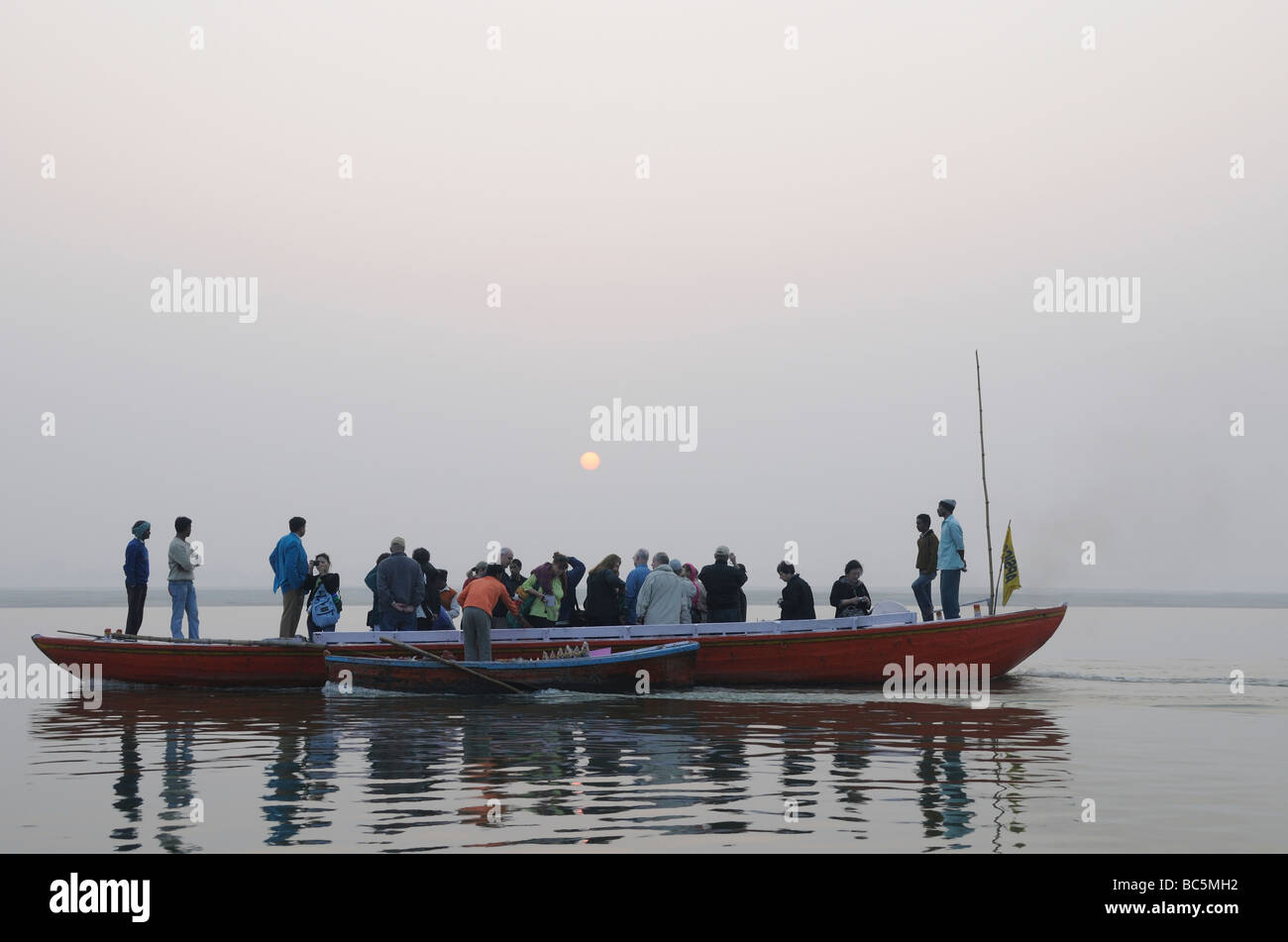 Touristen in einem langen Ruderboot beobachten den Sonnenaufgang über den Fluss Ganges. Varanasi Stockfoto