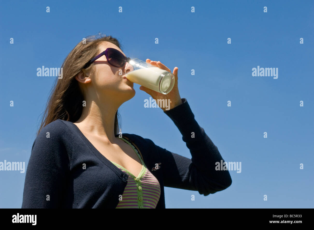 Kaukasische Mädchen (14) ein Glas frische Milch an einem sonnigen Tag mit blauem Himmelshintergrund. Stockfoto