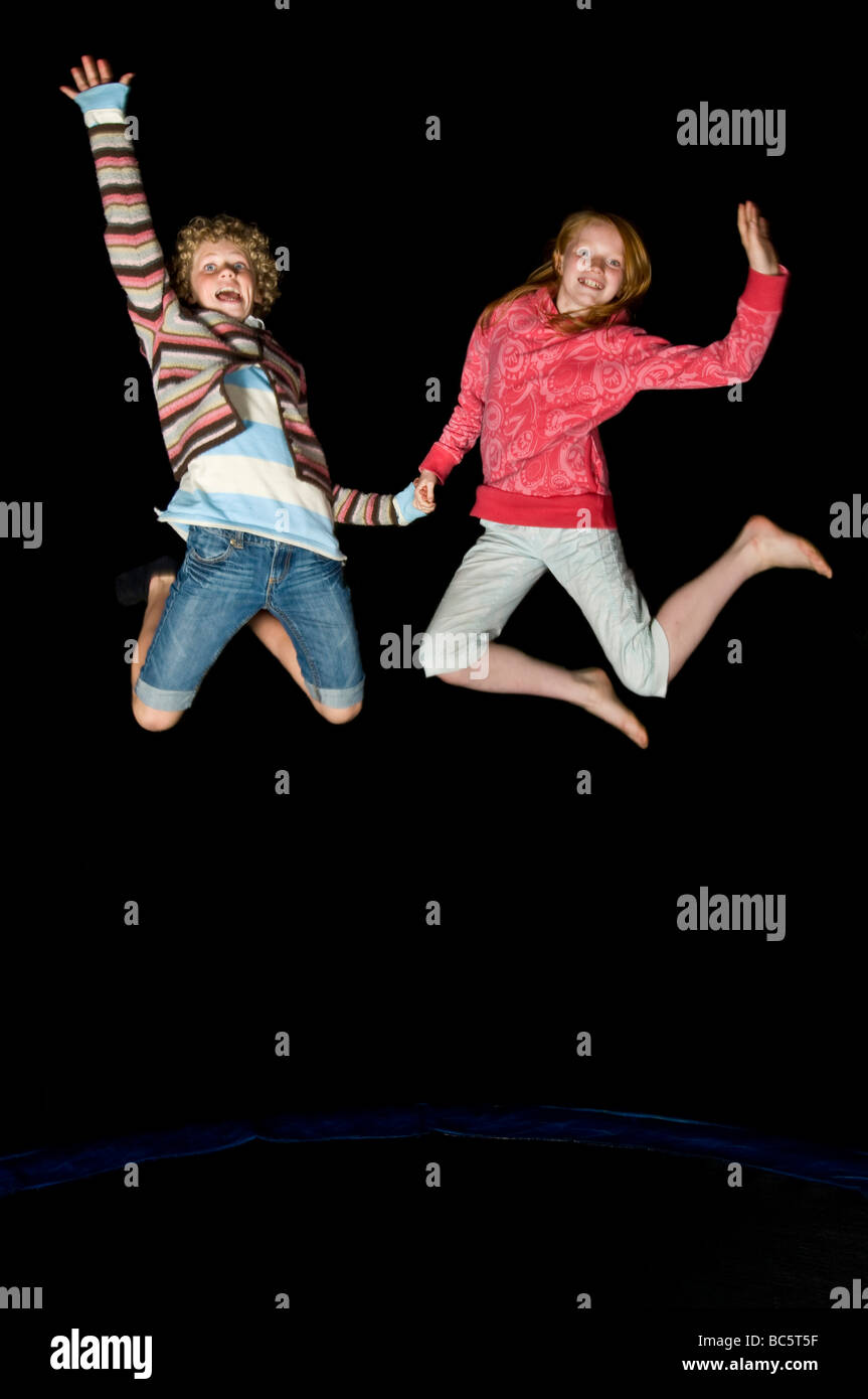 2 junge Teenager-Freundinnen springen auf einem Trampolin beim Lachen in der Nacht auf einem Geburtstag "Sleepover". Stockfoto