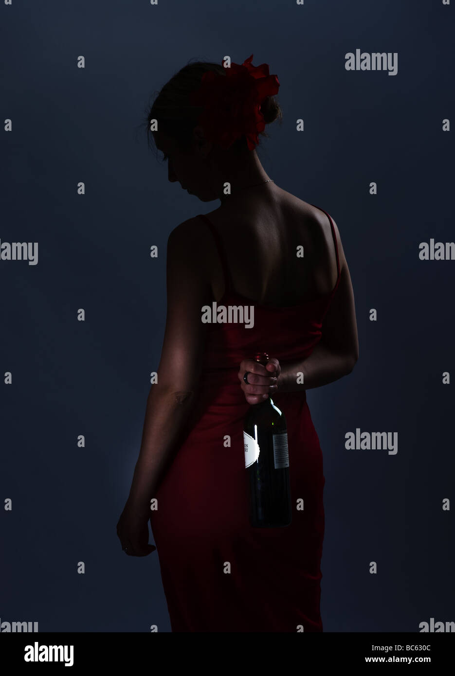 Porträt einer gut gekleideten jungen Frau eine Flasche Wein hinter ihrem Rücken versteckt Stockfoto