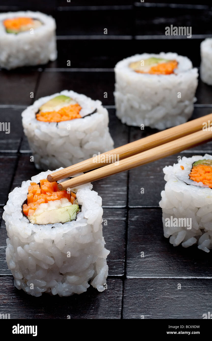 vertikale flachen Fokus Nahaufnahme von Sushi mit Stäbchen auf einem schwarzen Hintergrund aus Holz Stockfoto