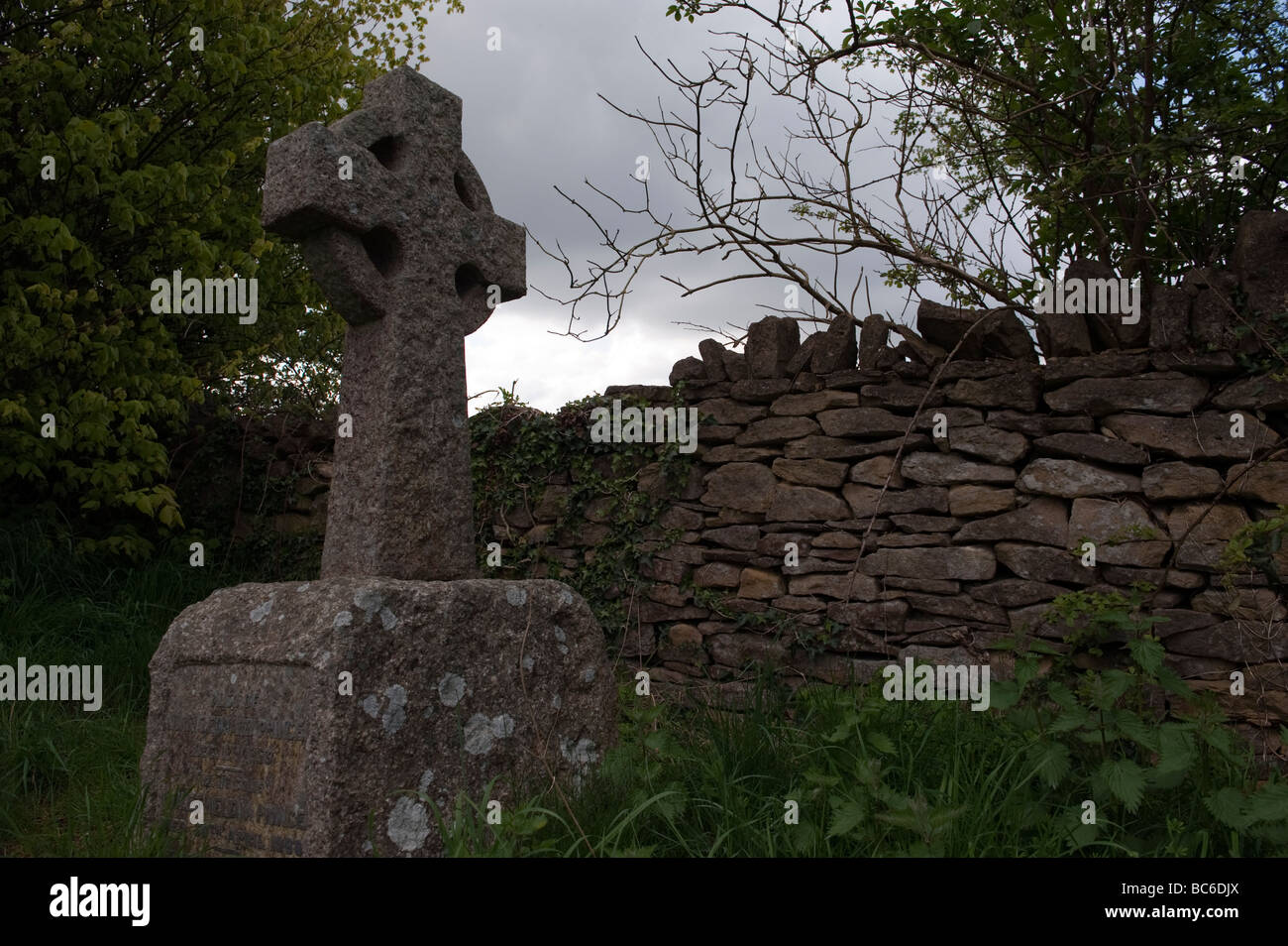 Atmosphärische und stimmungsvolle Pictue Stein Kreuz Grabstein gegen einen grauen Himmel und trocknen Steinmauer an Beckford Turm, Lansdown, Bath Stockfoto