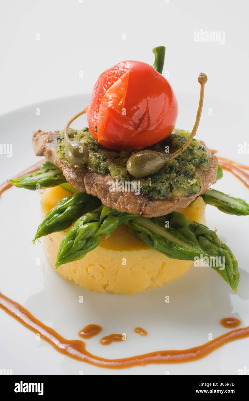 Schnitzel mit Kräutern, Kapern, Pfeffer & Spargel auf Polenta- Stockfoto