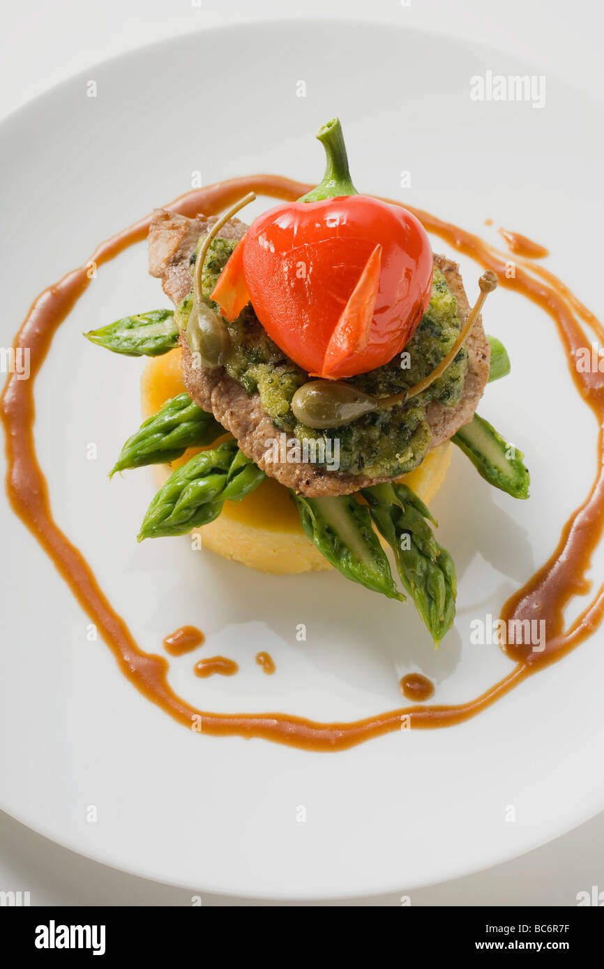 Schnitzel mit Kräutern, Kapern, Pfeffer & Spargel auf Polenta- Stockfoto