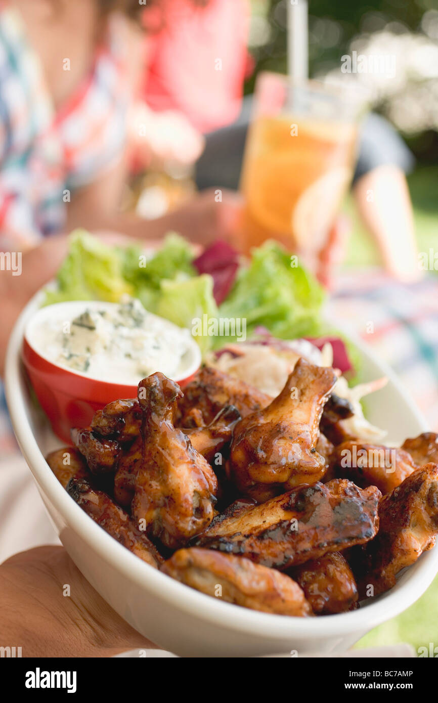 Hände halten Hähnchenflügel mit Salat, Menschen im Hintergrund- Stockfoto