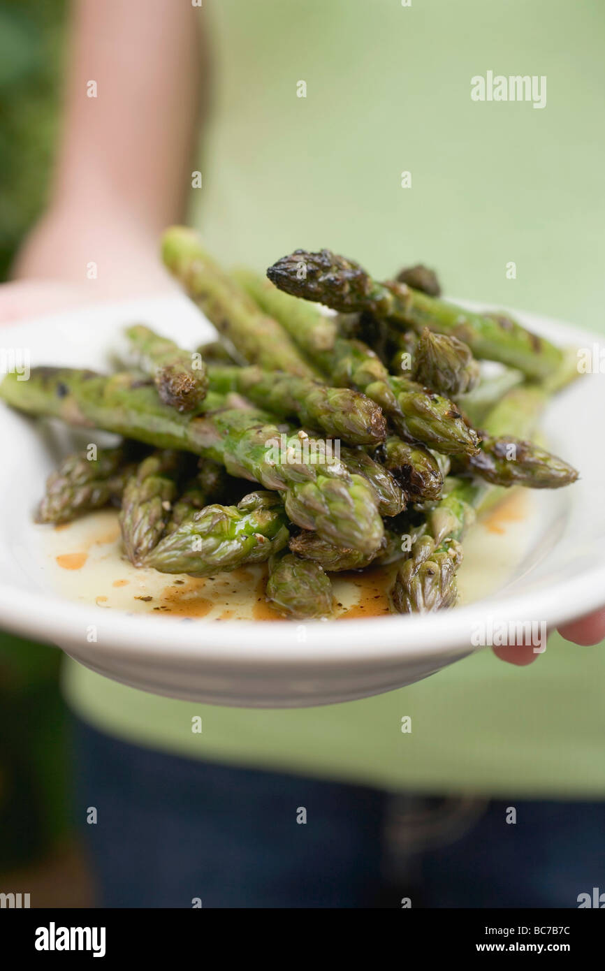 Person, die einen Teller mit gegrilltem grünem Spargel- Stockfoto