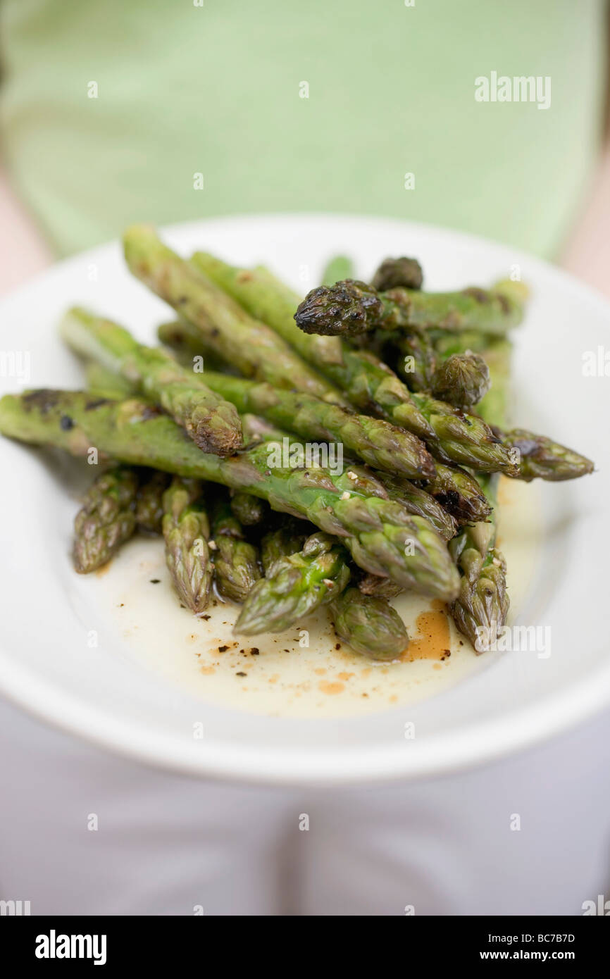Person, die einen Teller mit gegrilltem grünem Spargel- Stockfoto