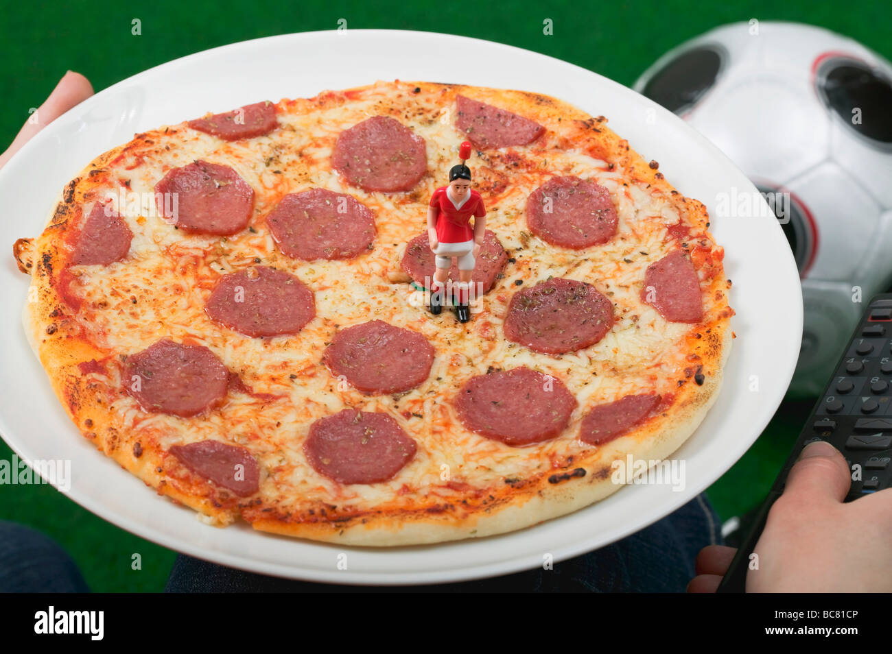 Hände halten Salami Pizza mit Spielzeug Fußballer und Fernbedienung - Stockfoto