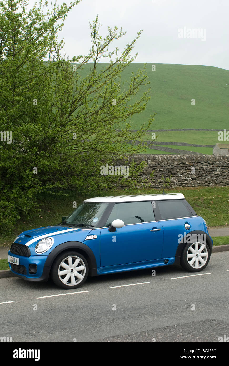 Blauen Mini Cooper s Auto an der Seite von der Straße in einem Dorf in der englischen Landschaft Stockfoto