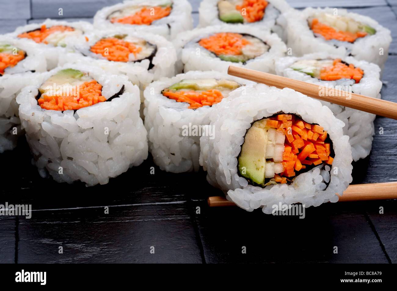 Ess-Stäbchen Sushi auf einem schwarzen Hintergrund strukturierte infront von mehr Sushi halten Stockfoto