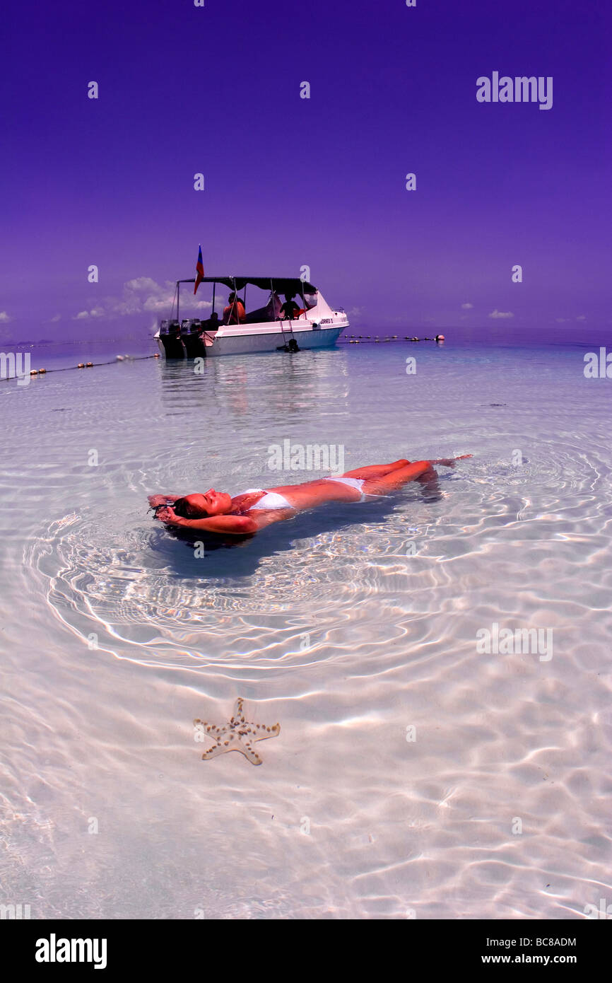 Mädchen in weißen Bikini im seichten Wasser über einem weißen Sand zu schweben. Boot im Hintergrund und Chocolate Chip Starfish Unterwasser Stockfoto