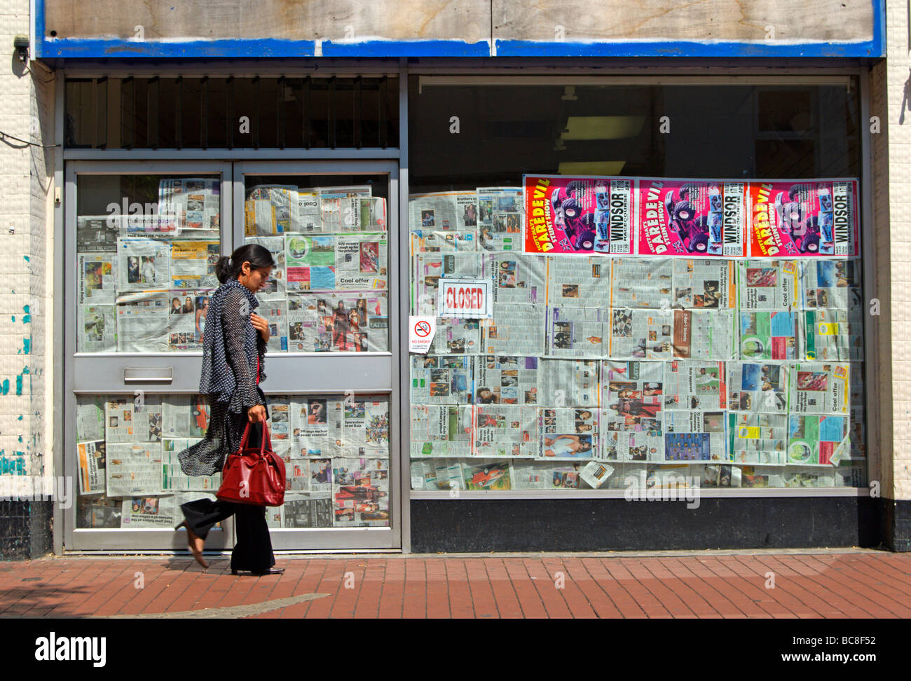 junge Frau der britischen asiatischen aussehen, vorbei an einem stillgelegten Shop, ihre Fenster, gesäumt von alten Zeitungen Stockfoto