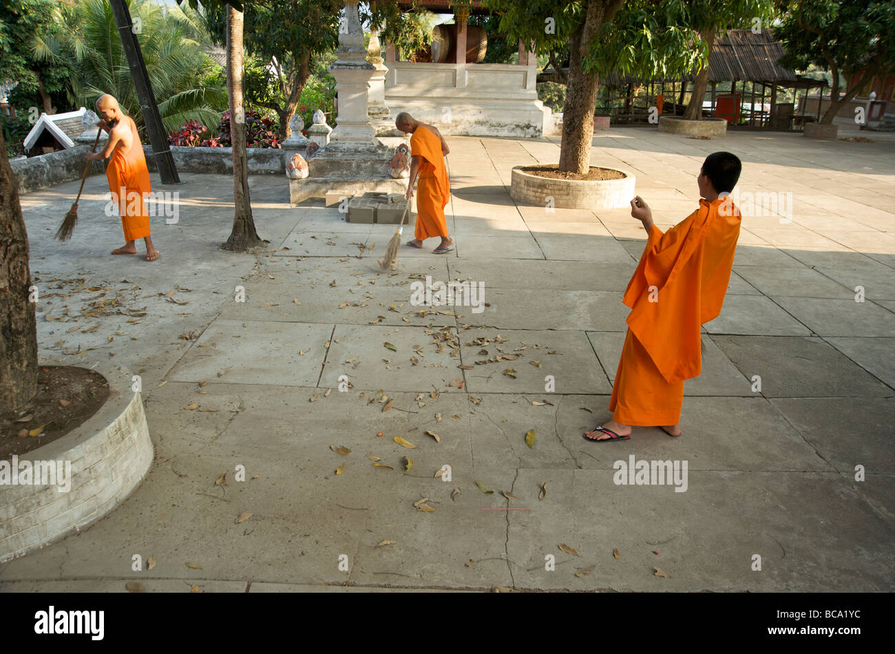 Drei buddhistische Mönche kehren die Gründe ihres Tempels in Luang Prabang Laos Stockfoto