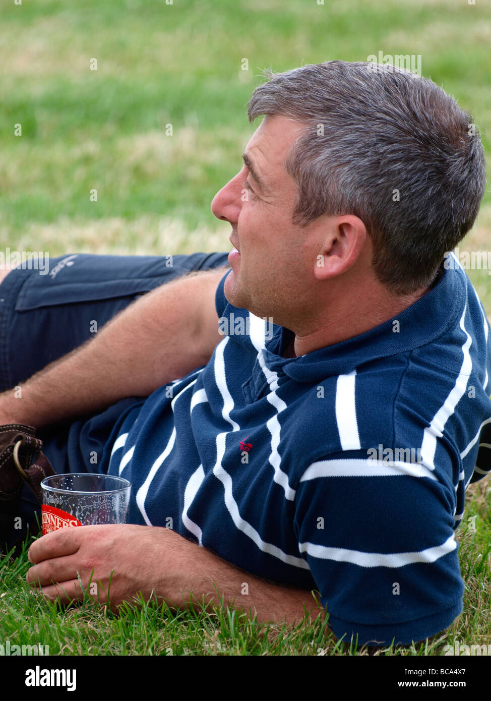Mann, die Verlegung auf dem Rasen mit einem Bier Stockfoto
