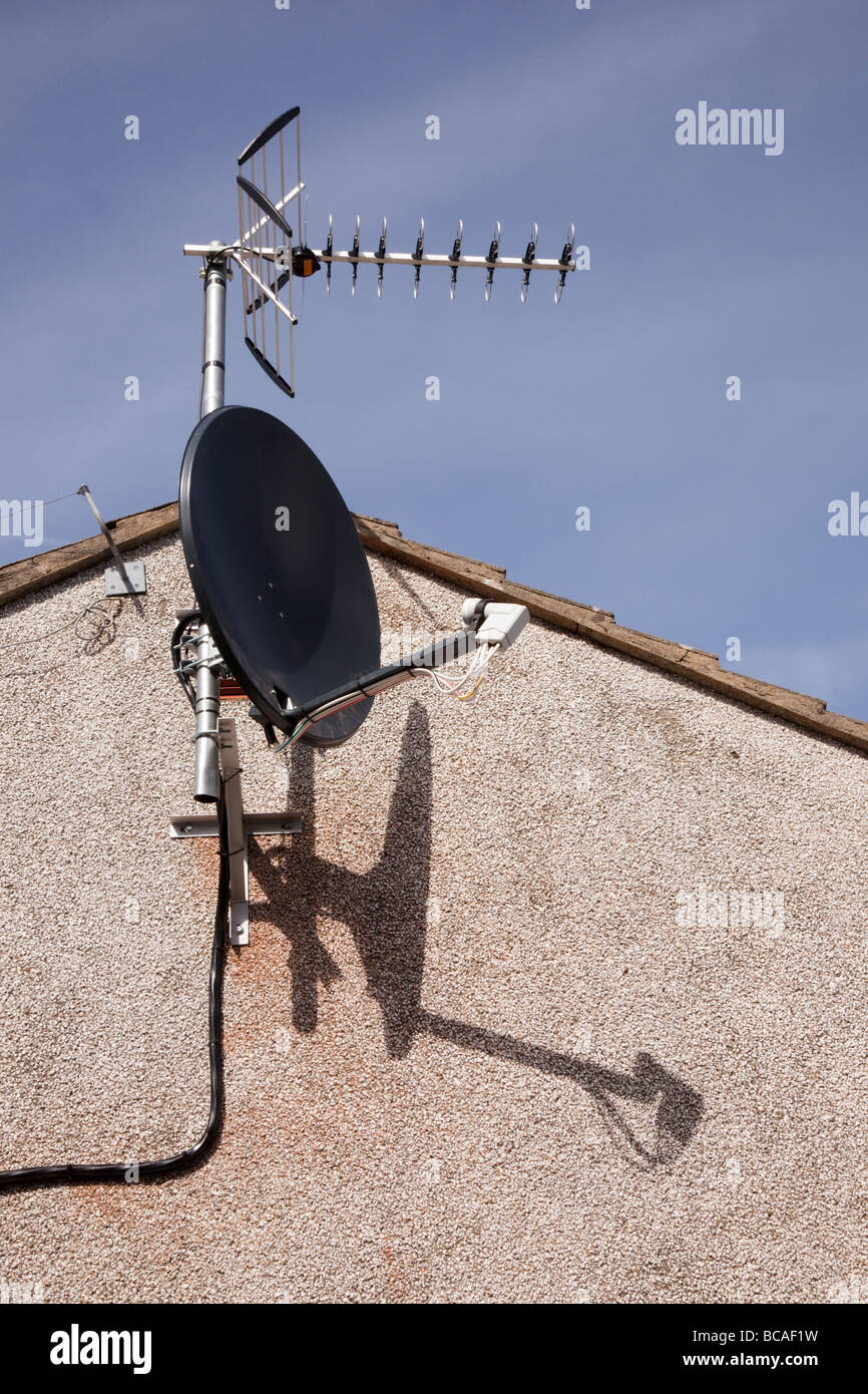 Großbritannien UK Digital Satellitenschüssel und TV-Antenne auf einem Haus gegen blauen Himmel Stockfoto