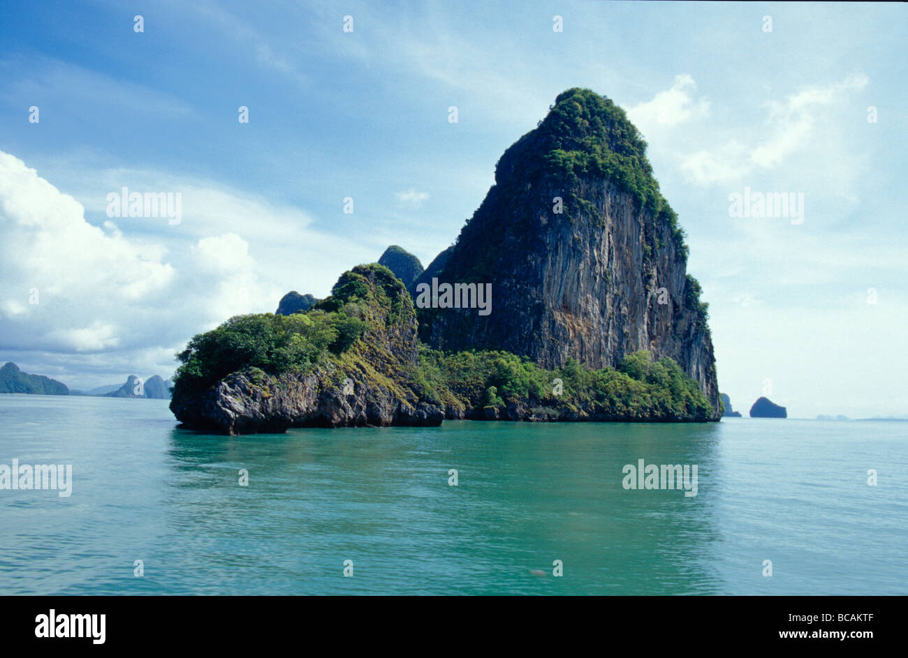 Eine schiere Kalksteininsel ergibt sich aus einem ruhigen Aqua grünen Meer. Stockfoto