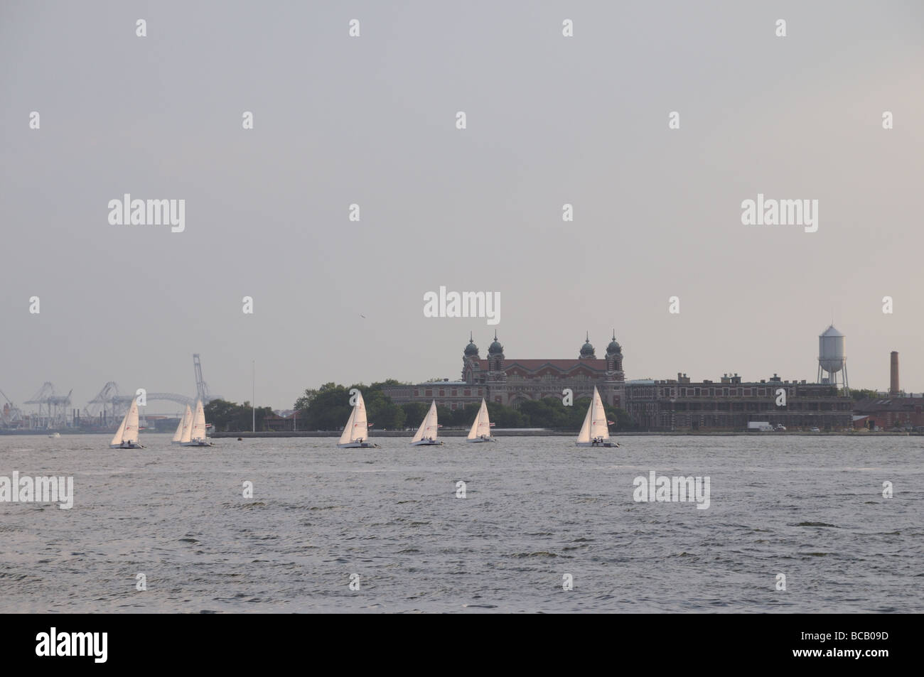 Ellis Island und Segelboote. In der Ferne sind die Bayonne Bridge und die Gantries von Port Elizabeth und Port Newark, NJ Stockfoto