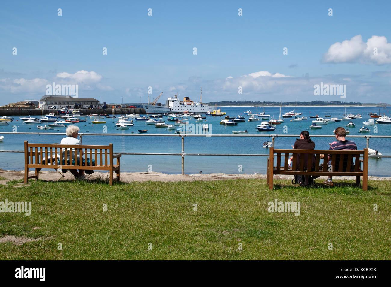 Menschen saßen auf Holgates Green sitzen Blick auf St. Marien Hafen und die Scllionian, Isles of Scilly, Cornwall UK. Stockfoto