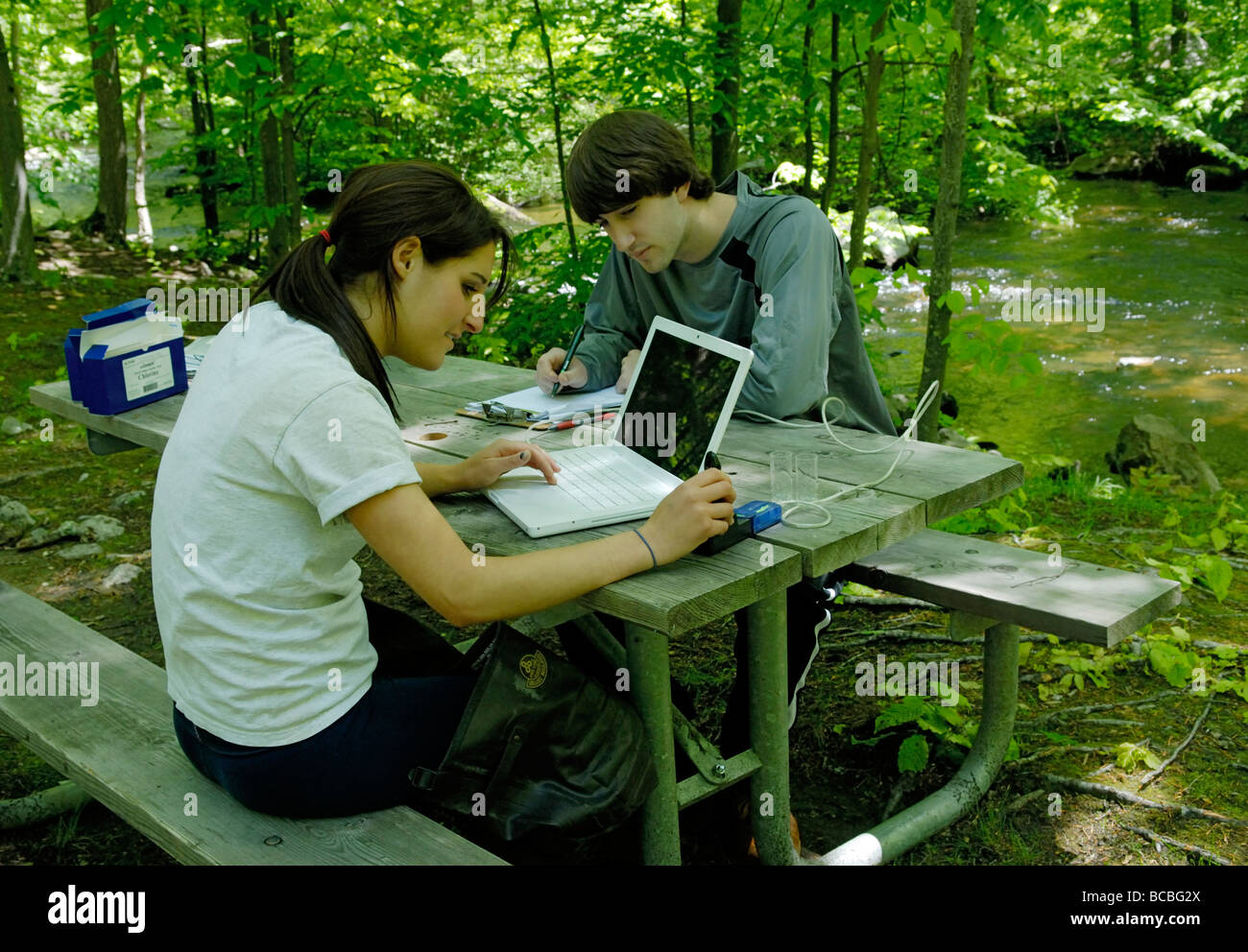 Zwei Teenager, die mit einem Laptop verbunden Sensor zur Messung der Wasserqualität eines Streams Stockfoto