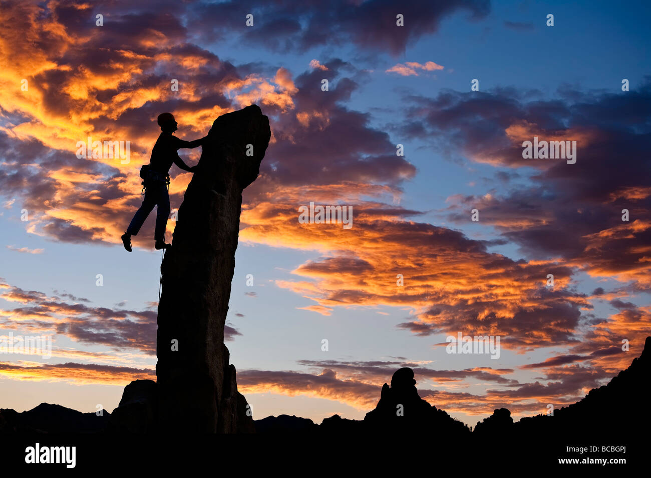 Bergsteiger ist am Rande abhebt, als er auf den Gipfel des eine Nadel dünnen Rock Turmspitze Kämpfe Stockfoto