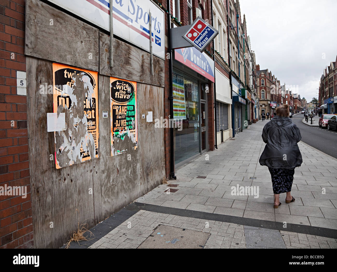 Frau zu Fuß vorbei an Brettern vernagelt Closed Shops in Haupt Straße Barry Wales UK Stockfoto