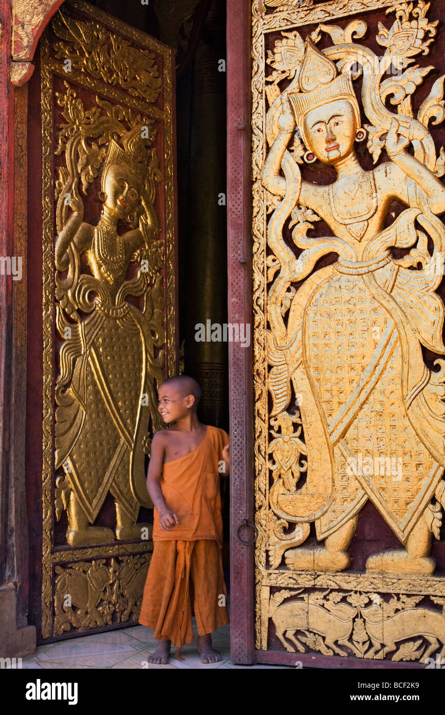 Myanmar, Burma, Wan-seeing.  Ein junger Novize neben die kunstvoll geschnitzten und vergoldeten Türen. Stockfoto