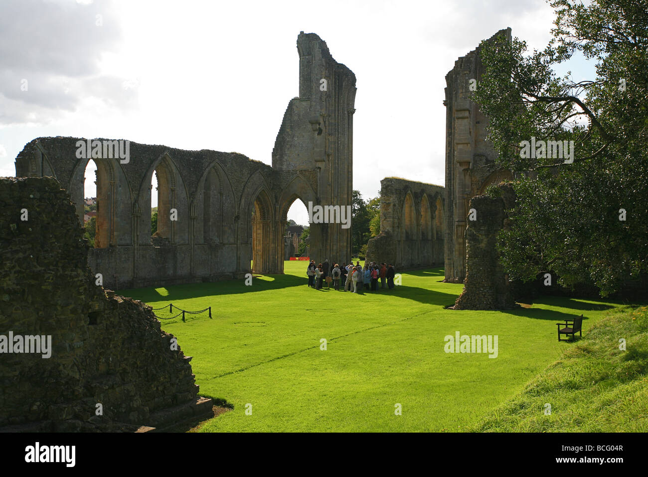 Eine Gruppe von Besuchern bekommen eine Führung von Glastonbury Abbey Ruinen, Somerset, England, UK Stockfoto