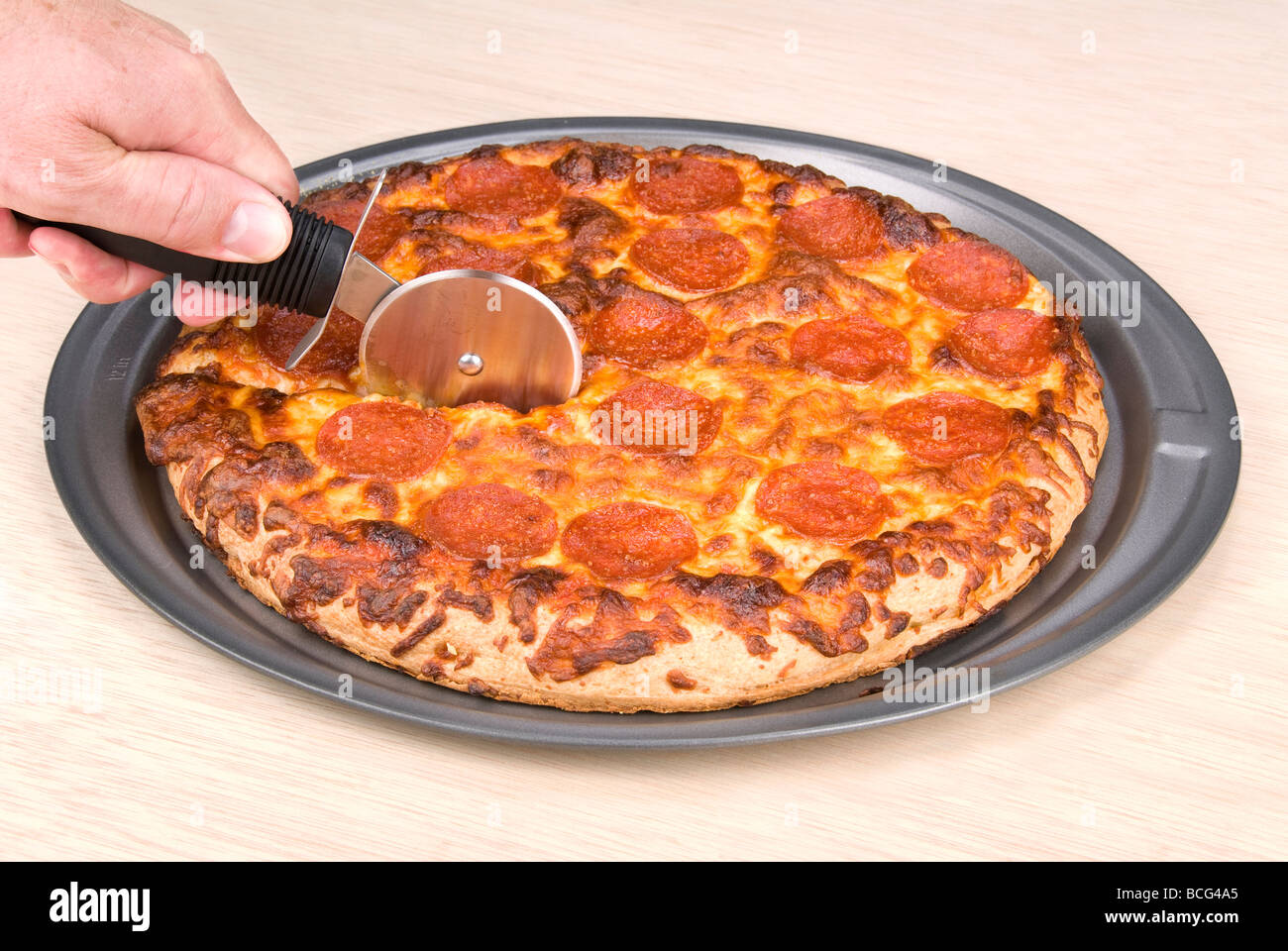 Ein Koch schneidet einer Peperoni-Pizza, dass s frisch aus dem Ofen Stockfoto