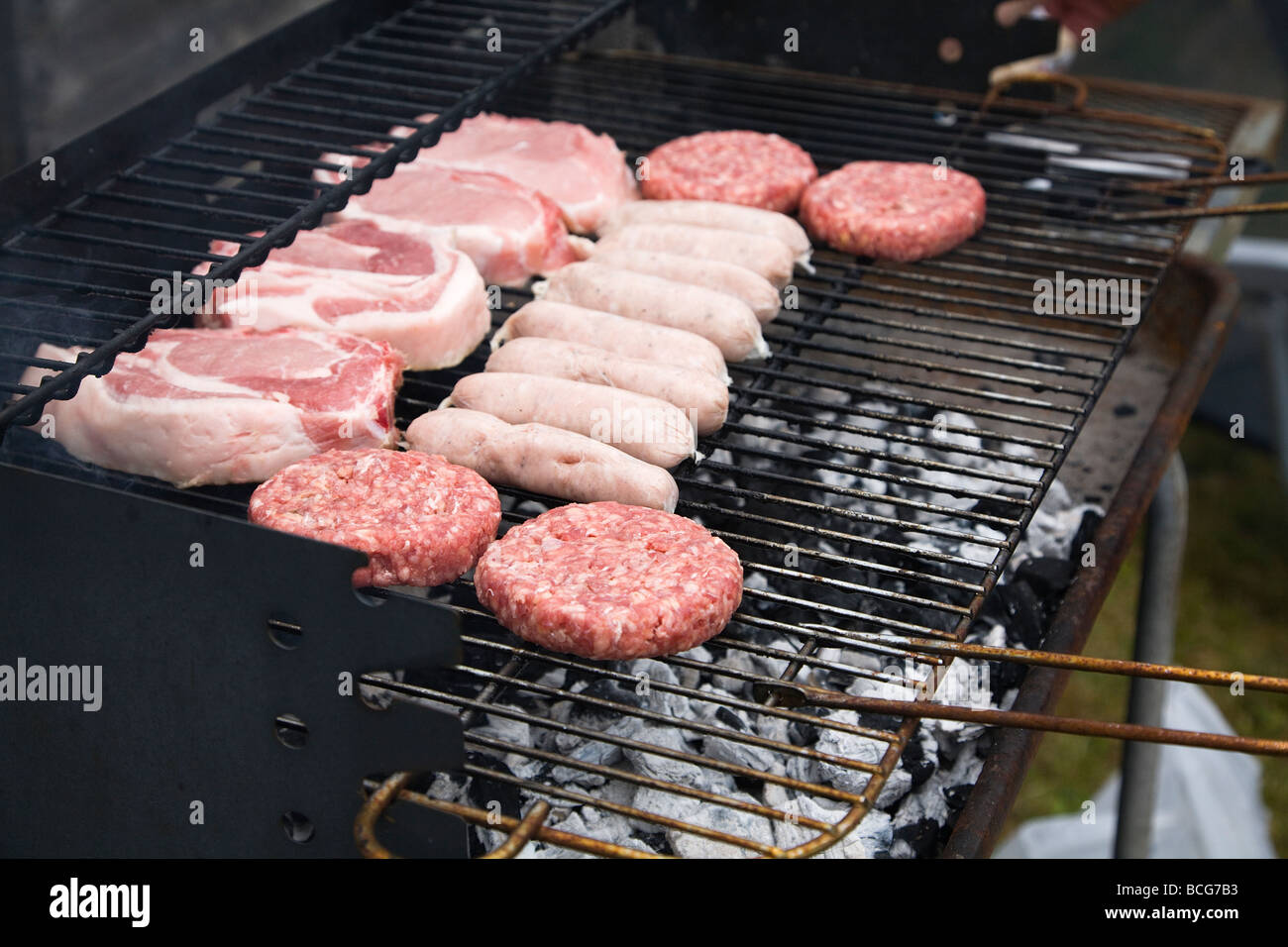 Frisches rohes Fleisch, Burger, Würstchen und Schweinefleisch Koteletts, Kochen auf ein Barbecue-Grill. England, UK. Stockfoto