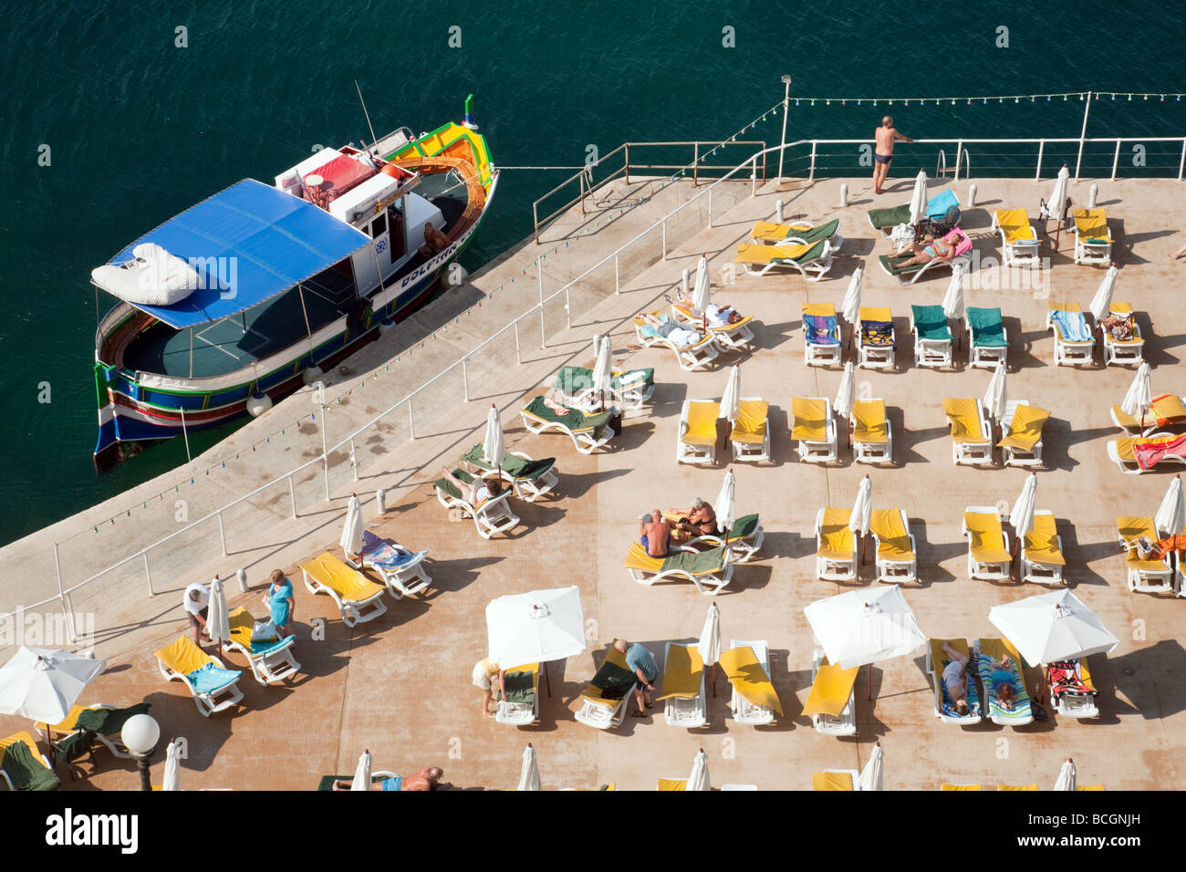 Draufsicht der Touristen, ein Luzzu (traditionelle maltesische Boot) und Sonnenliegen, Hotel Fortina, Sliema, Malta Stockfoto