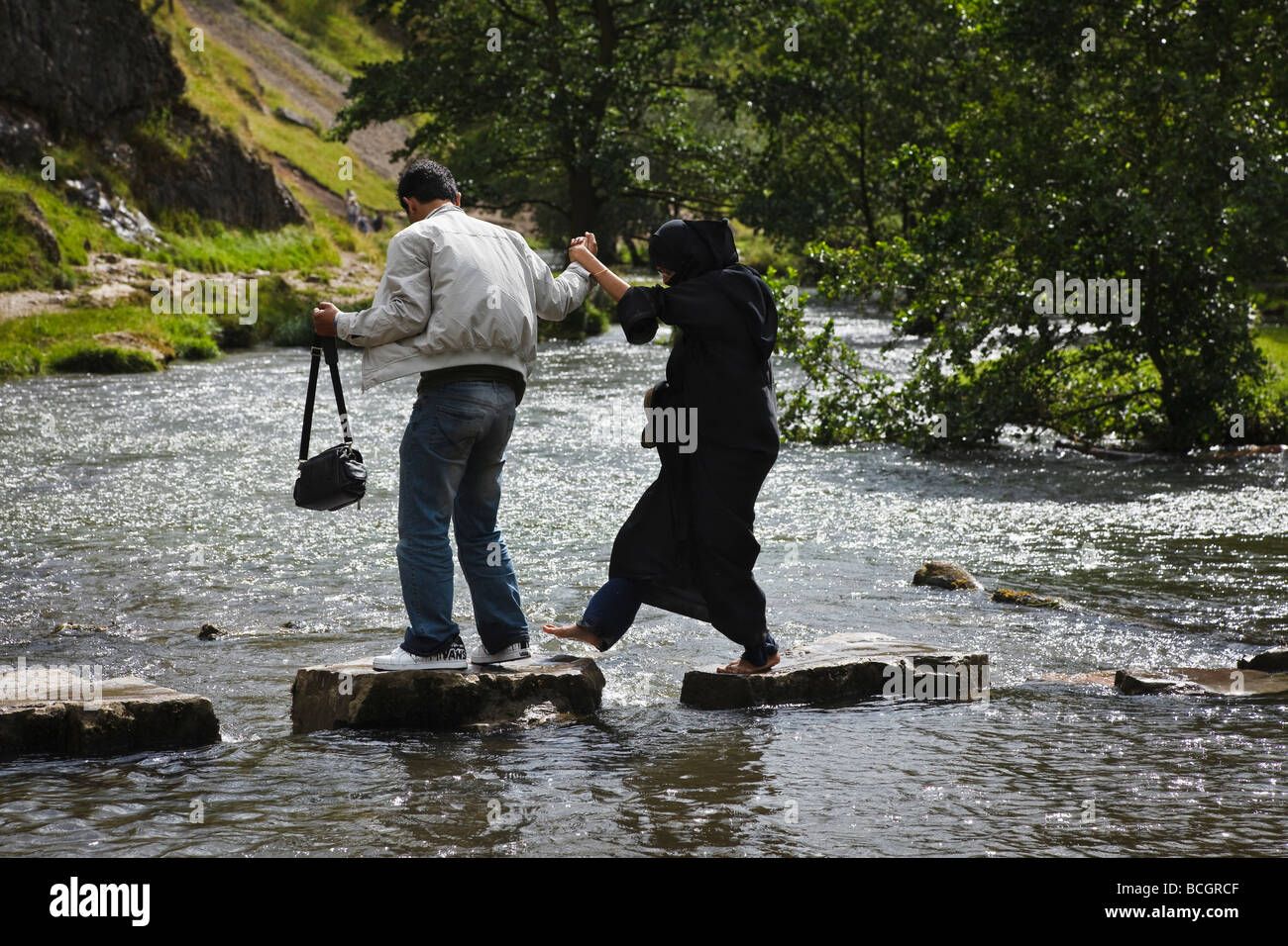 Muslimische Frau tragen von Burka über das Stepping Stones in Dovedale geholfen wird, von ihrem Ehemann, Peak District, Derbyshire Stockfoto