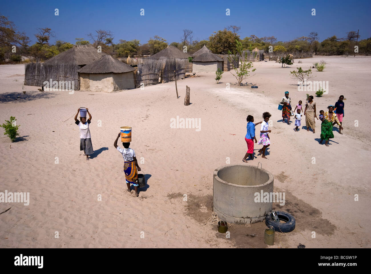 Afrikanische Womans Wasserholen mit anderen Einwohnern des Dorfes im Hintergrund, Caprivi Strip Gegend, Namibia Stockfoto