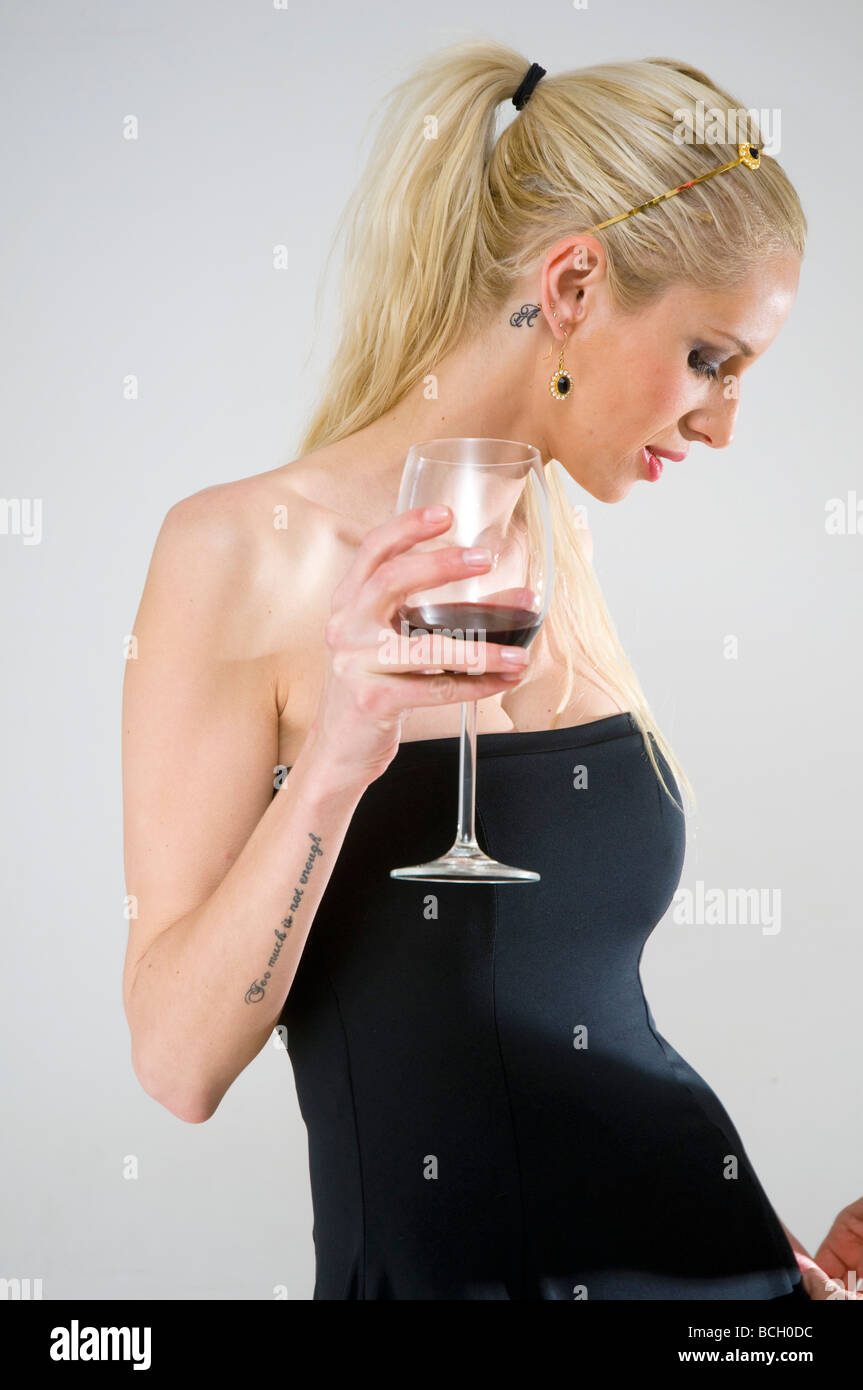 Junge weibliche blonde Modell Mitte der zwanziger Jahre mit einem schwarzen Abendkleid trinken Rotwein auf weißem Hintergrund Stockfoto