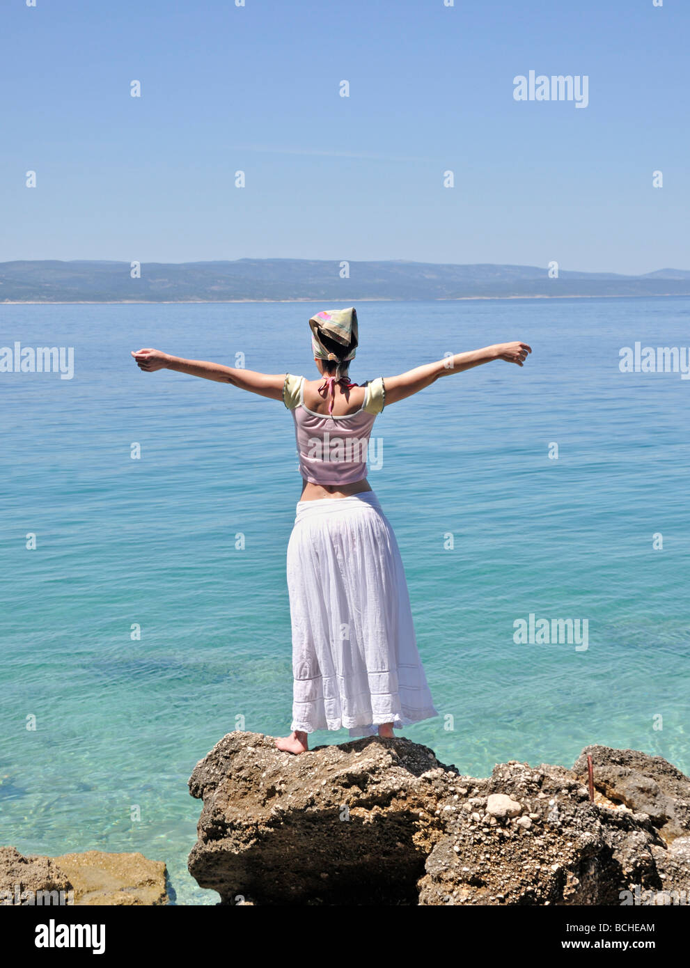 Junge Frau, die auf Felsen von Ozean erhobenen Armen Stockfoto