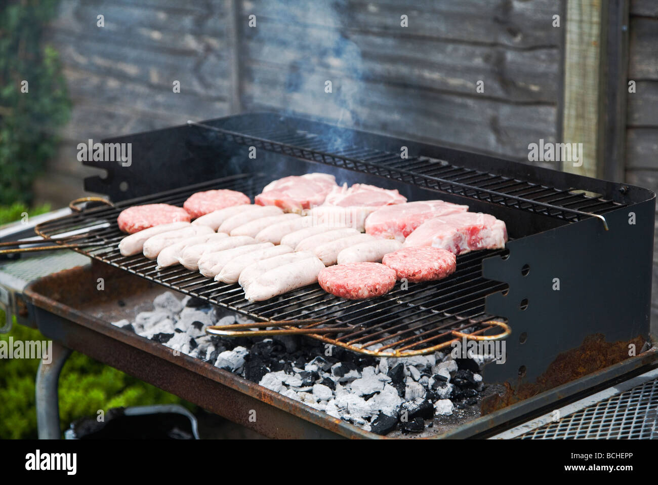 Frisches rohes Fleisch, Burger, Würstchen und Schweinefleisch Koteletts, Kochen auf ein Barbecue-Grill. England, UK. Stockfoto