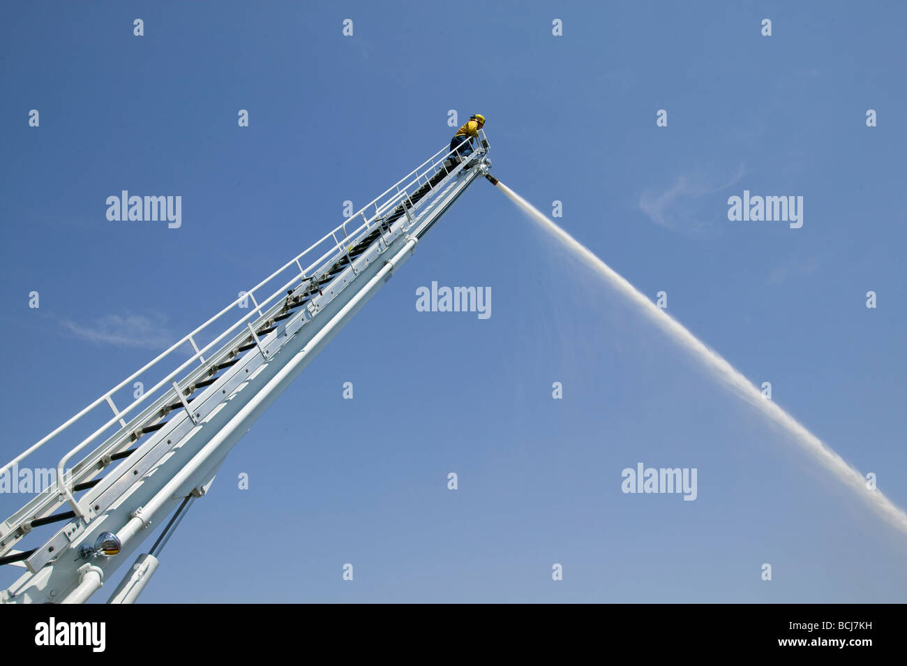 Feuerwehrmann Feuerwehrmann auf hohen Leiter mit Feuerwehrschlauch Spritzen Wasserstrahl gegen Himmel Stockfoto