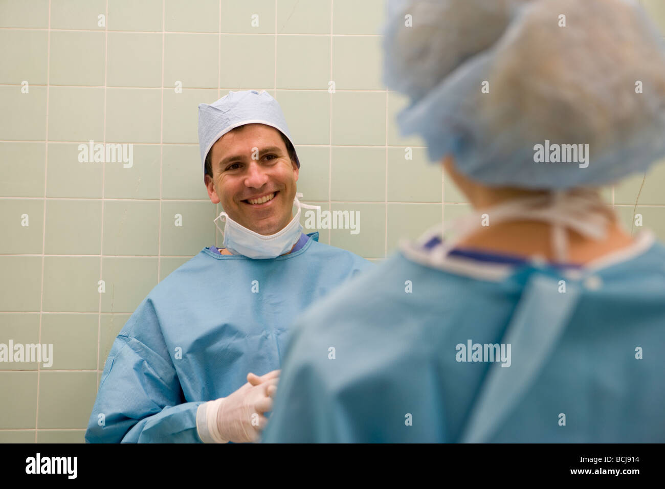 Kaukasische männlichen Chirurg/Arzt in blauen chirurgische Peelings gelehnt grünen Fliesen zu Fuß, mit zweiter Person zu sprechen. Stockfoto