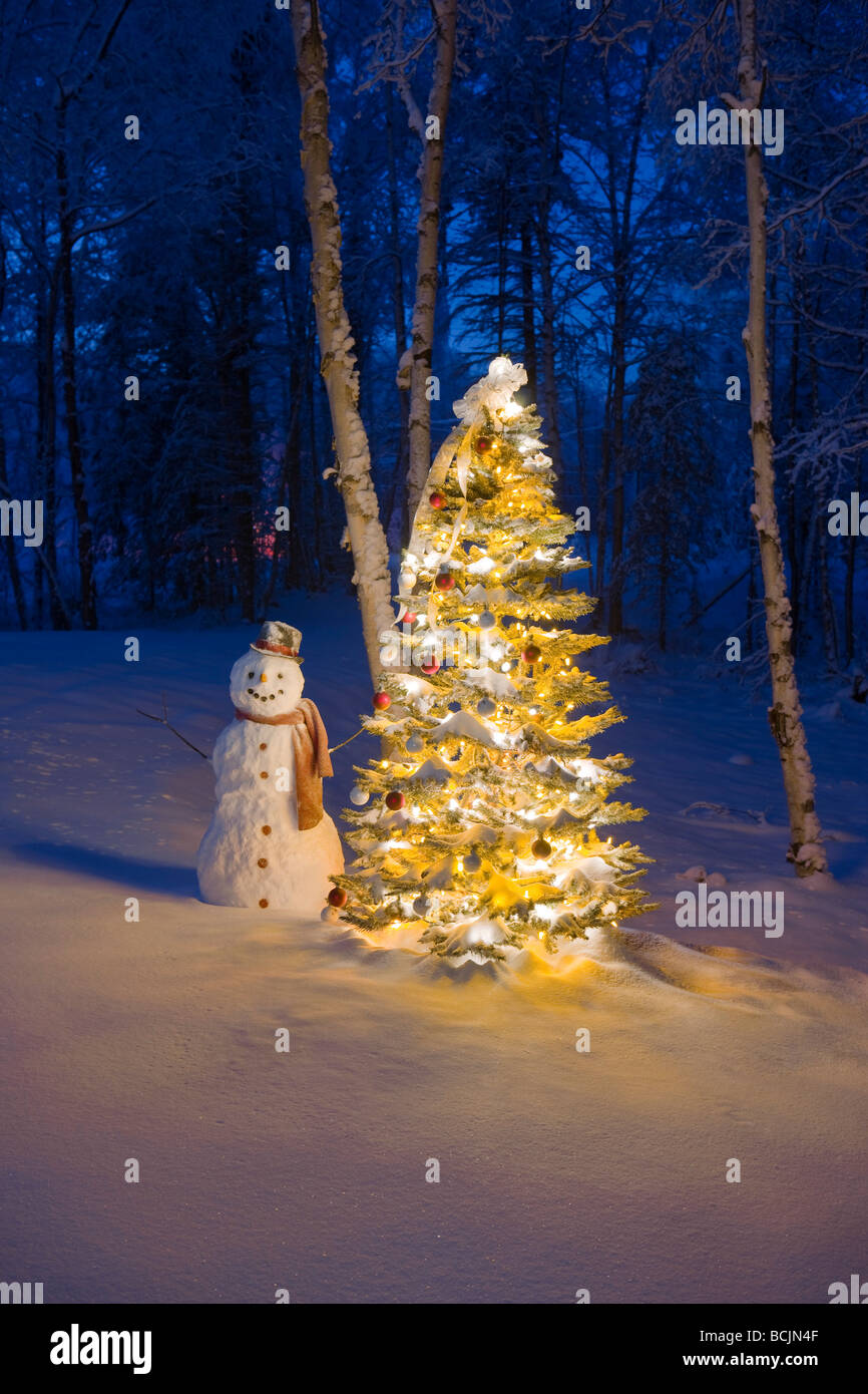 Schneemann mit rotem Schal und schwarzen Zylinderhut stand neben einem Weihnachtsbaum im Schnee bedeckt Birkenwald, Winter Stockfoto
